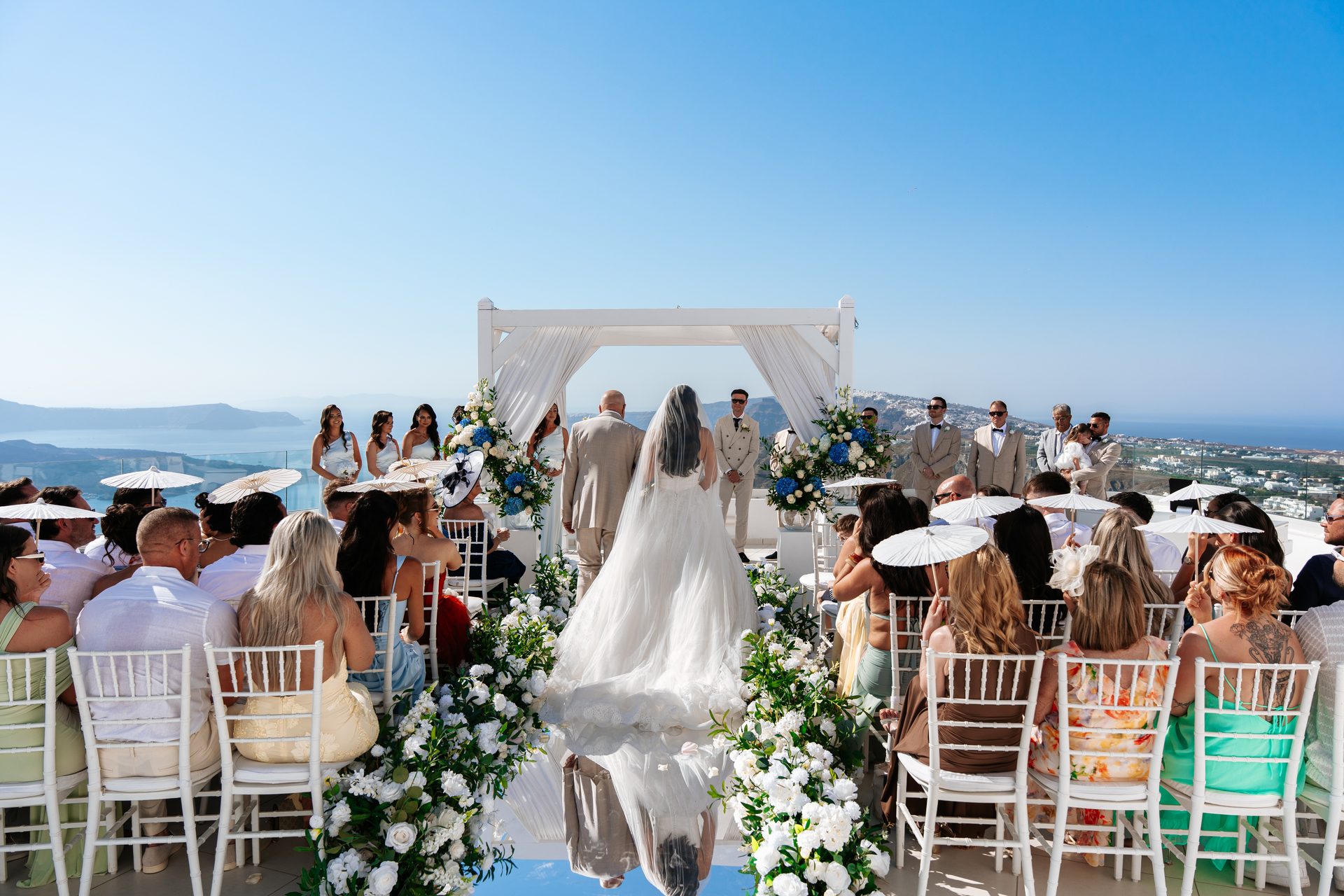 Bride walking down a mirrored aisle towards the caldera at a Santorini clifftop wedding