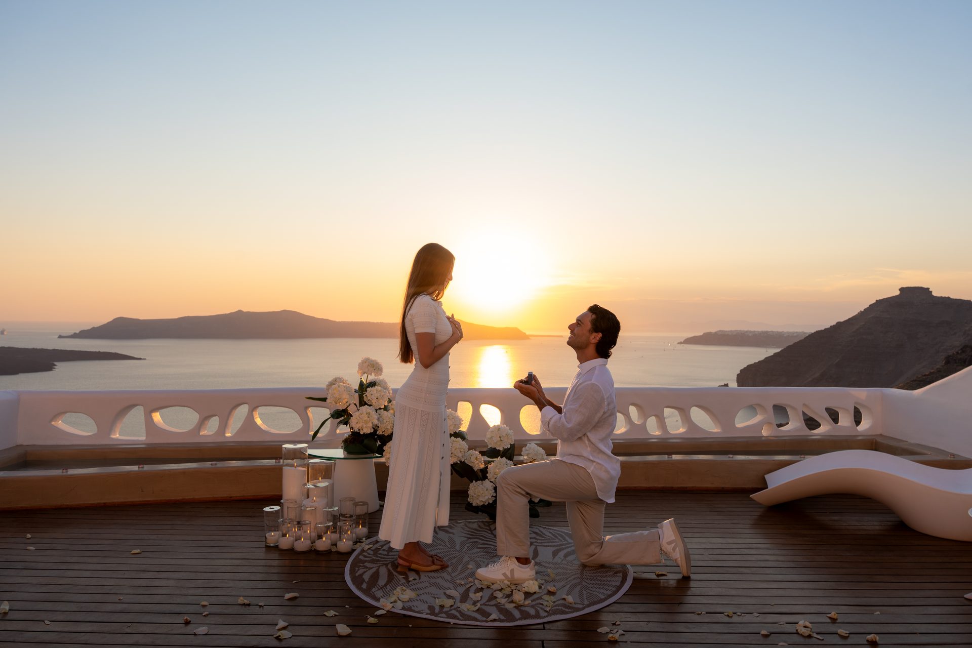 Man kneeling to propose on a Fira terrace as the sun sets over the Santorini caldera