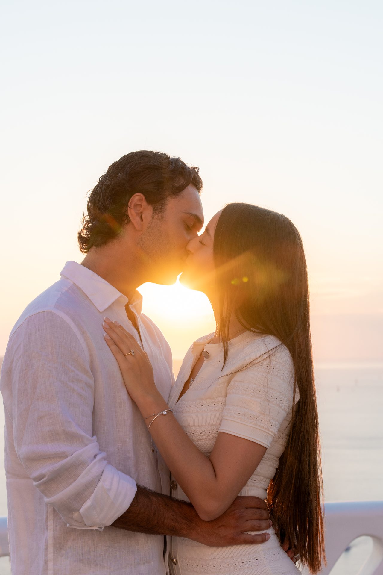 Newly engaged couple kissing with the setting sun between them, Fira, Santorini