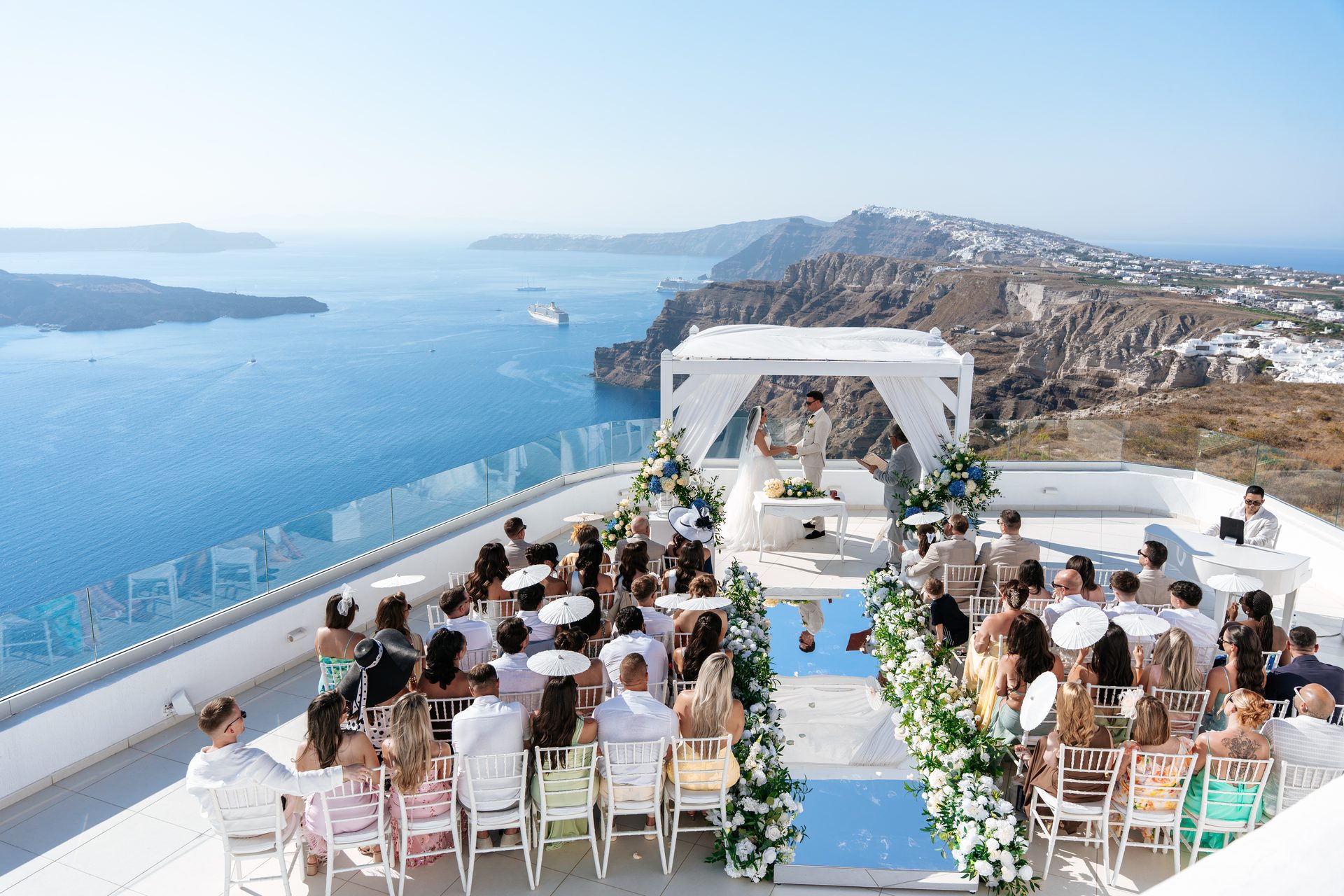 Santorini wedding ceremony seen from above with the caldera and Aegean behind