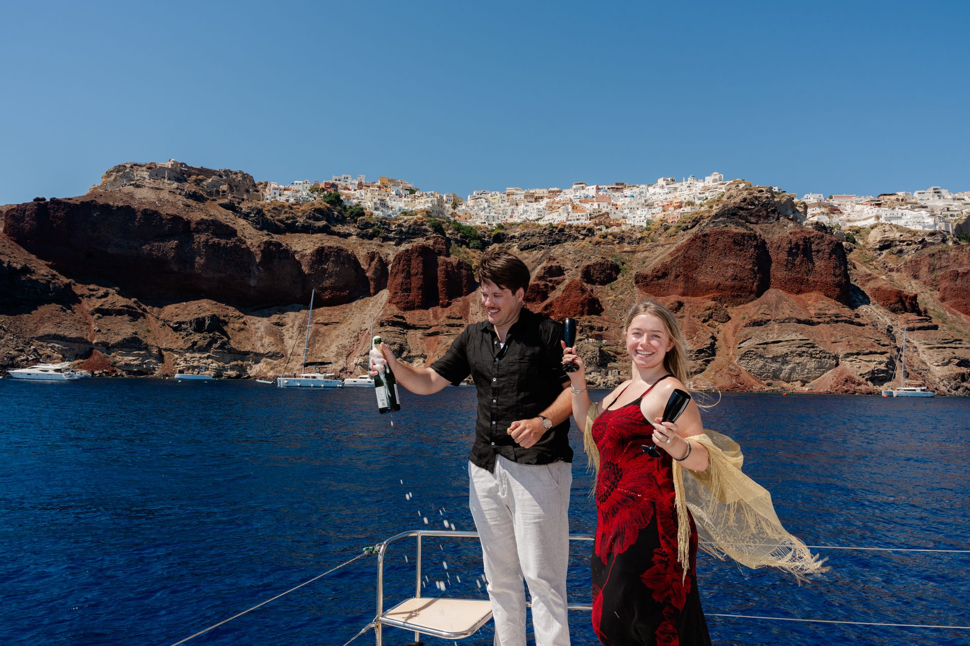 Popping champagne on a catamaran after a successful proposal on the Santorini caldera
