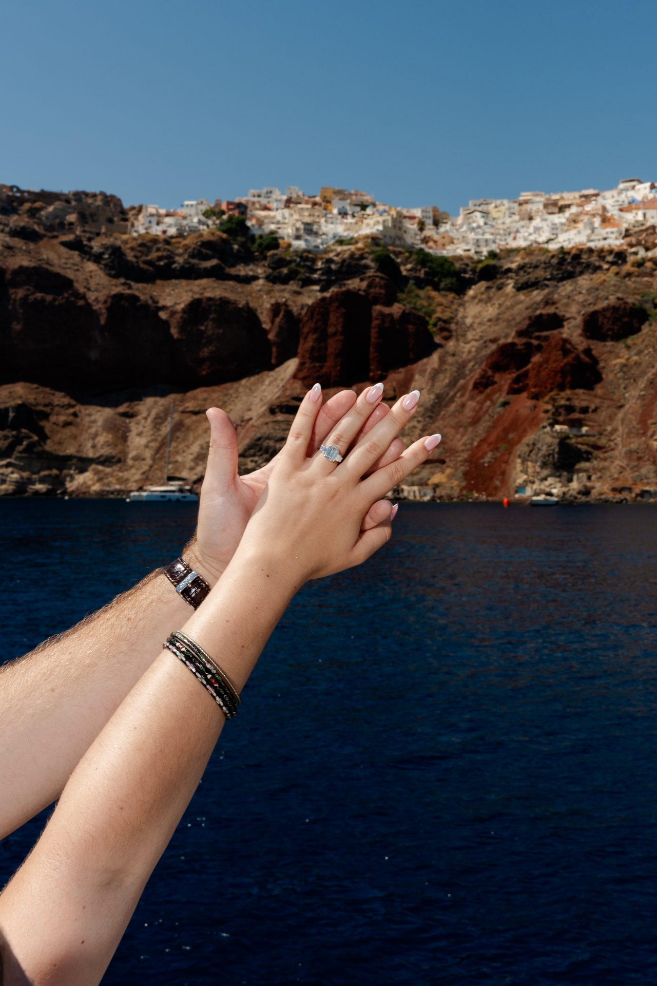 Engagement ring held up against the Oia cliffs from a catamaran, Santorini