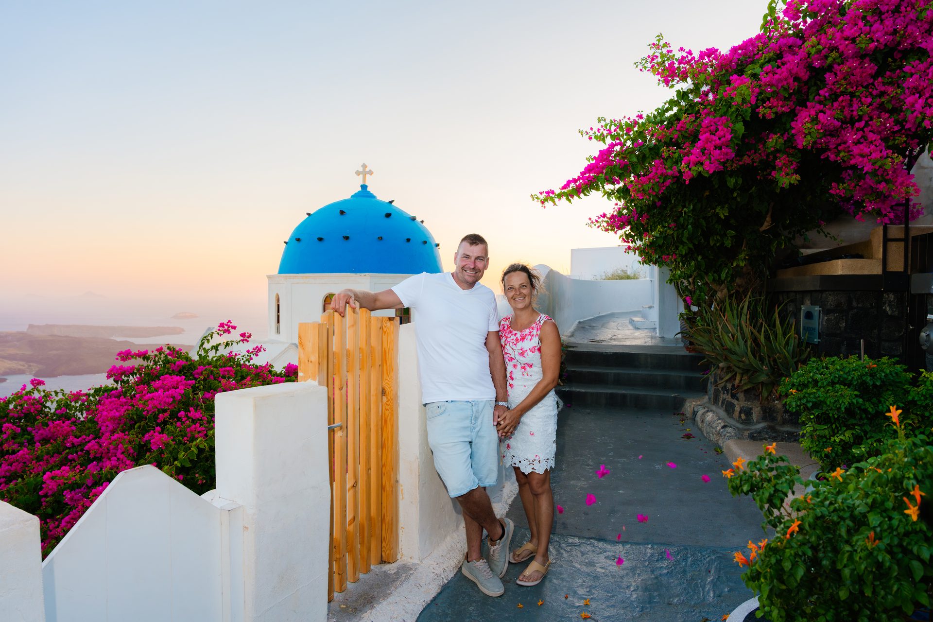 Engaged couple at the blue-domed church with pink bougainvillea in Oia, Santorini