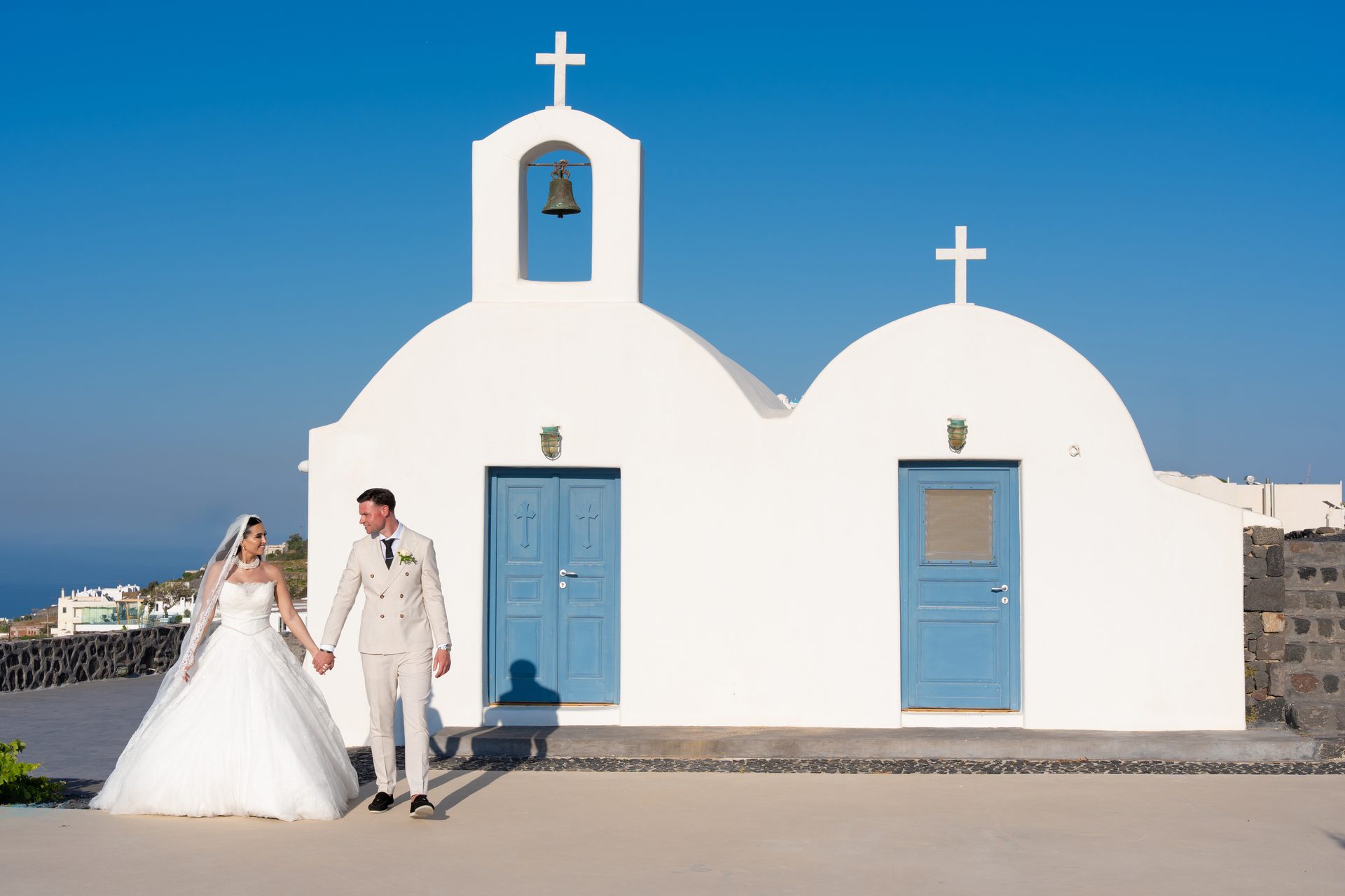 Bride and groom holding hands in front of a white chapel with blue doors, Santorini