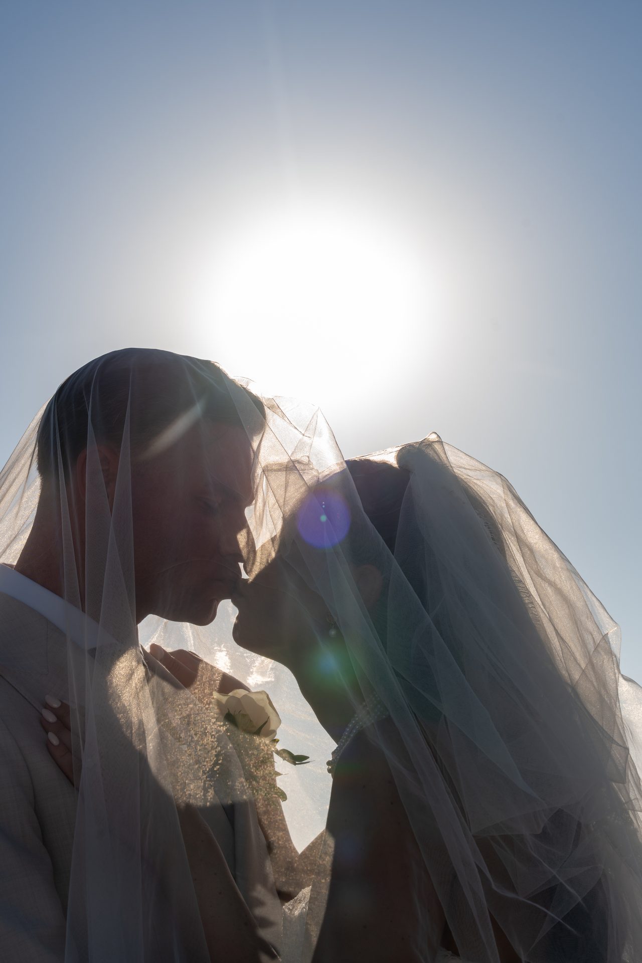 Sun shining through the bride's veil as the couple kiss, Santorini wedding portrait