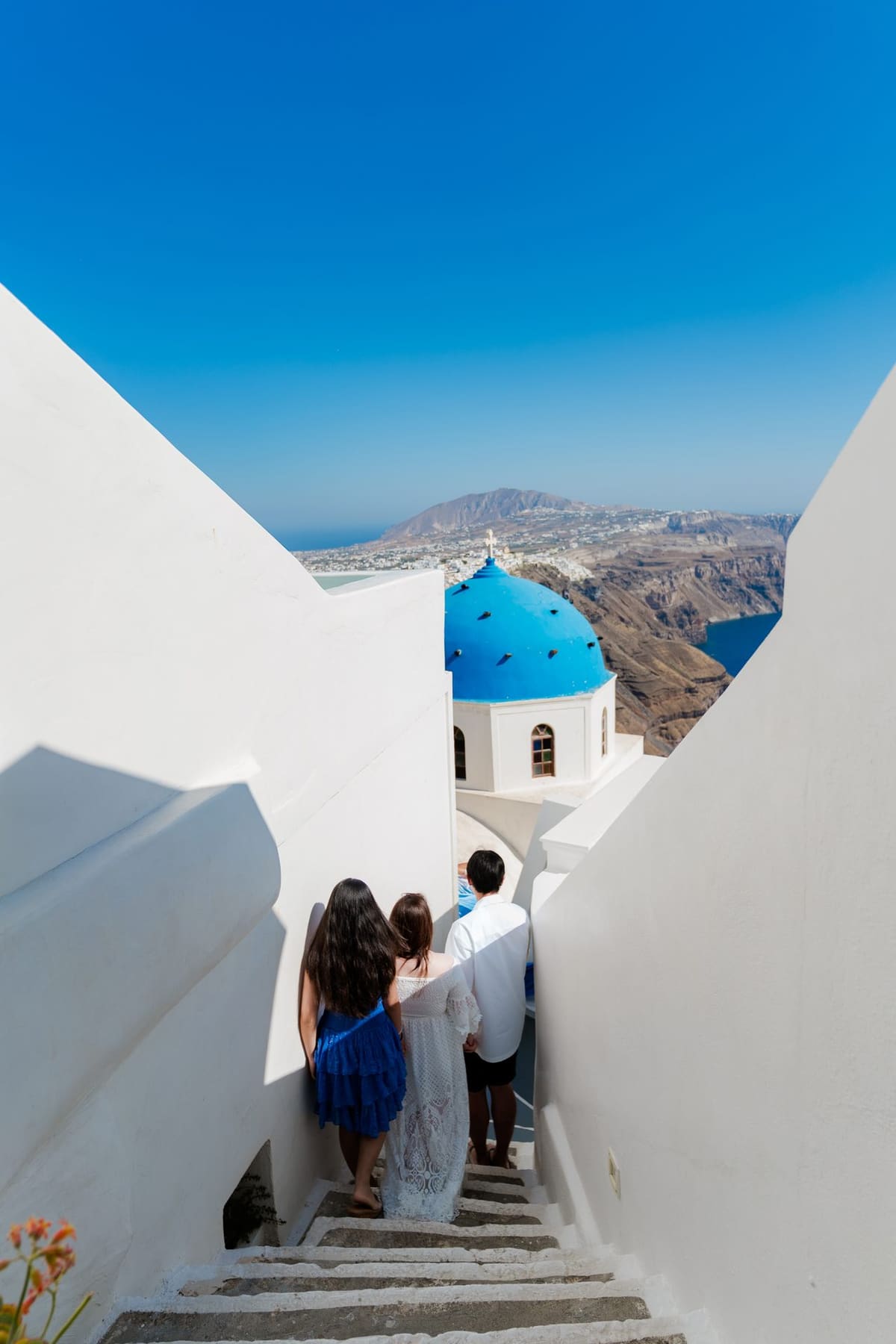 Family walking down the white steps beside the blue dome of the Anastasi church, Imerovigli