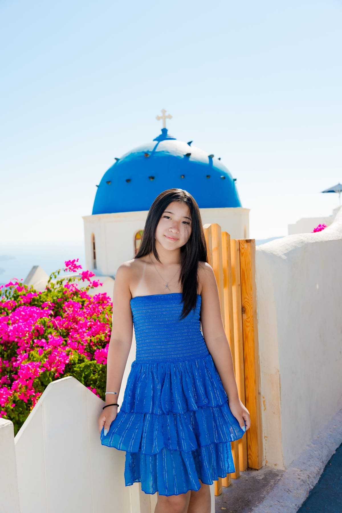 Teenage daughter in a blue dress beside the blue dome of Oia, Santorini family session