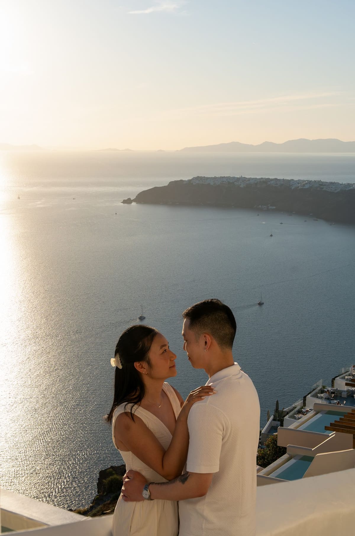 Couple embracing on a terrace in Imerovigli with the sun glittering on the caldera
