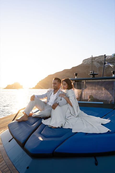 Just-engaged couple lying on the catamaran cushions as the sun sets over the Santorini caldera