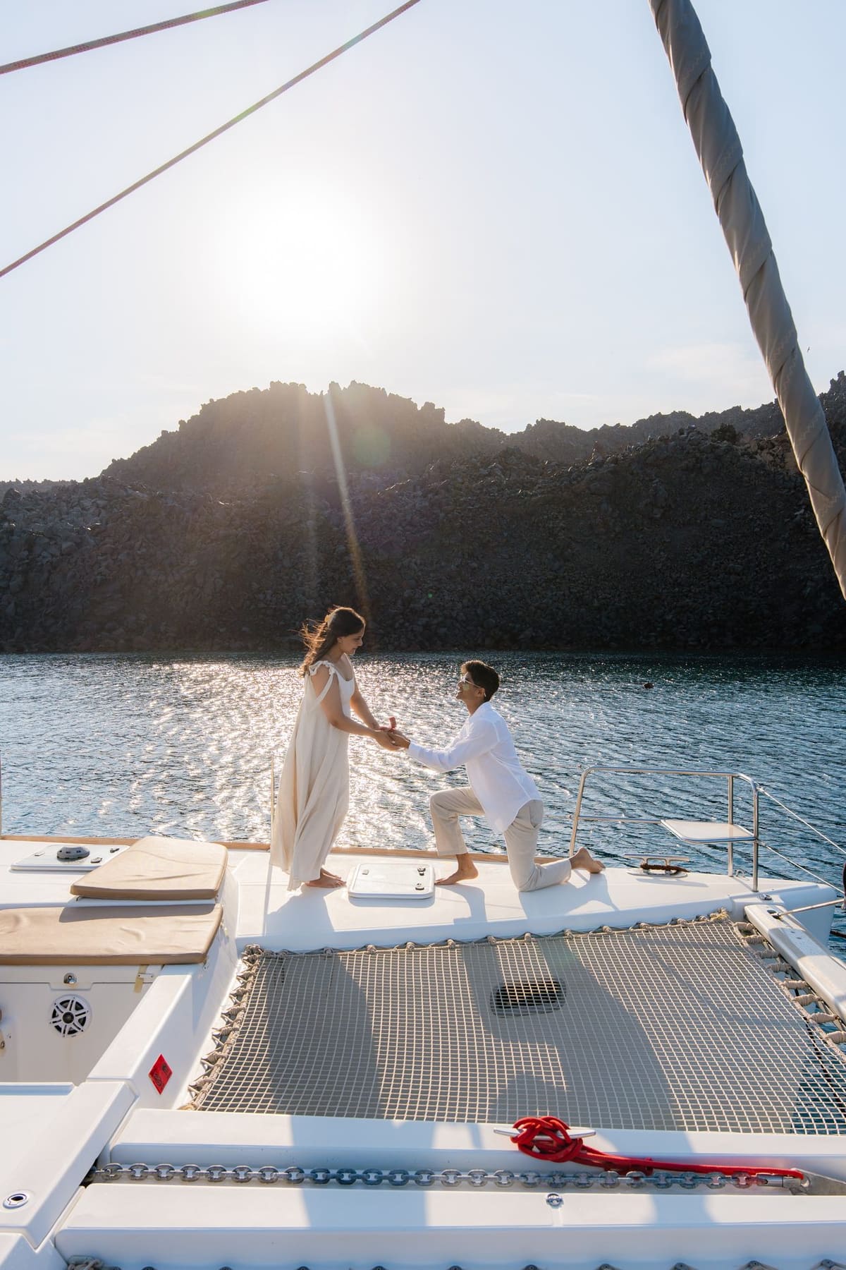 Couple on the catamaran bow with the volcano island and low sun, Santorini