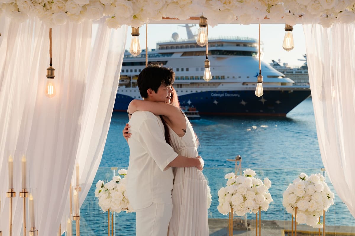 Couple embracing under a white flower canopy with a cruise ship in the bay, Fira, Santorini