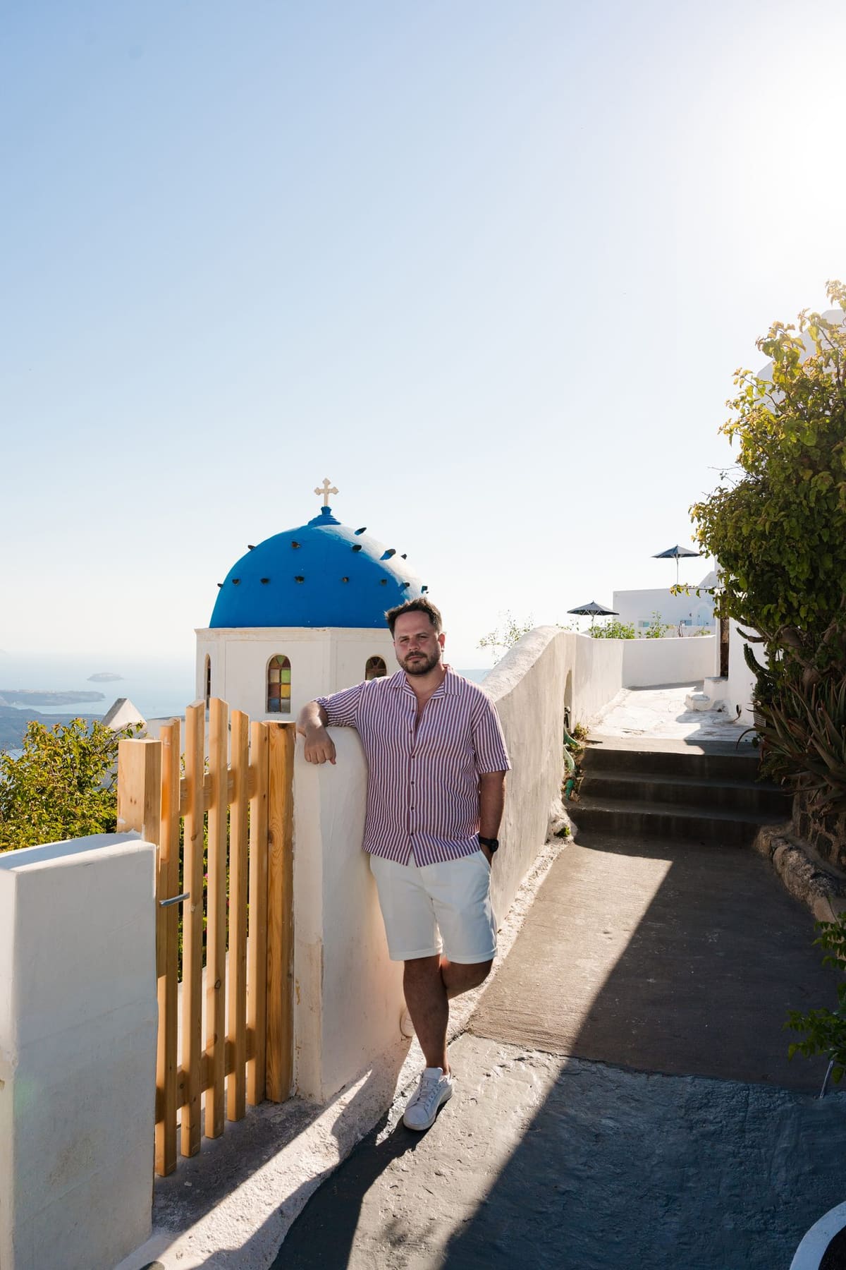 Couple at the wooden gate of a blue-domed chapel in Imerovigli, caldera behind