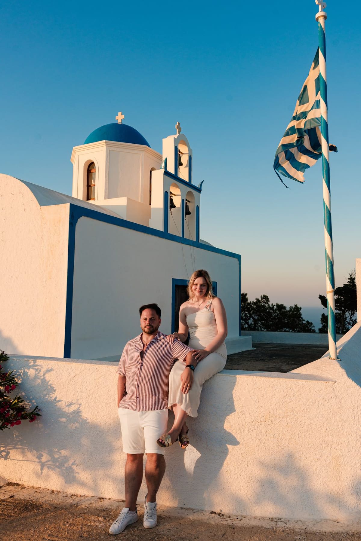 Couple below a blue-domed church with a Greek flag flying, Imerovigli, Santorini