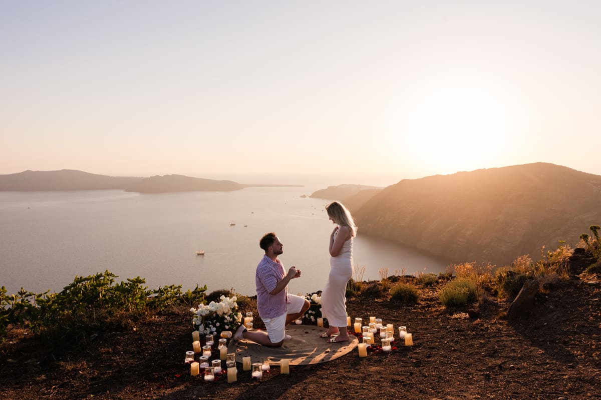 Man kneeling among candles on a cliff above the Santorini caldera at sunset