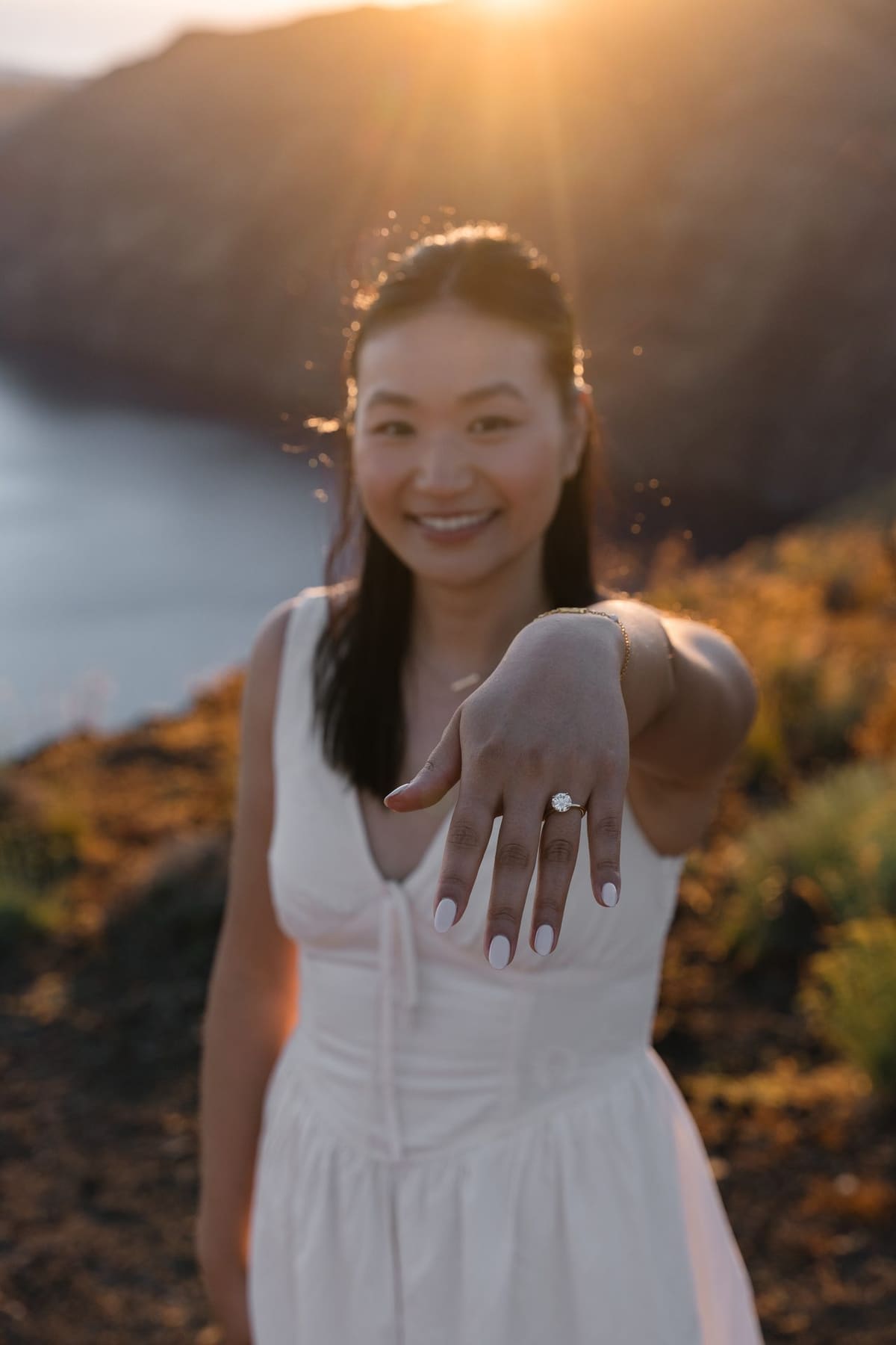 Woman showing her new engagement ring with the Santorini caldera glowing behind her