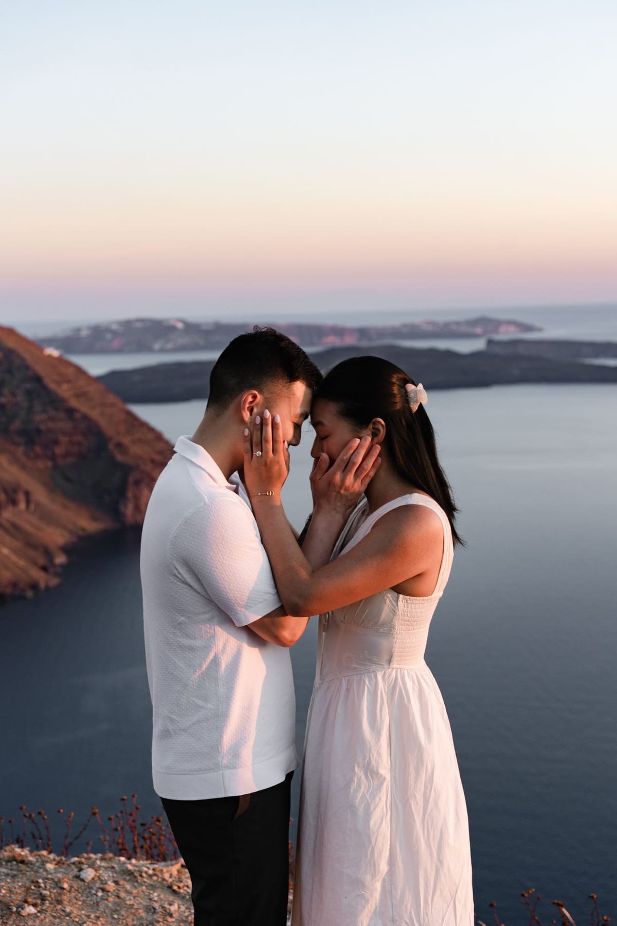 Couple touching foreheads after the proposal, caldera and sunset behind, Santorini