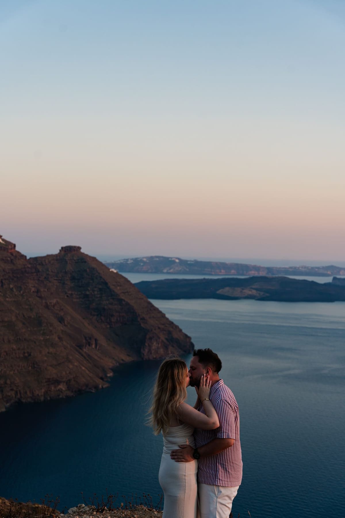 Engaged couple on the cliff with the caldera and volcano in the last light, Santorini