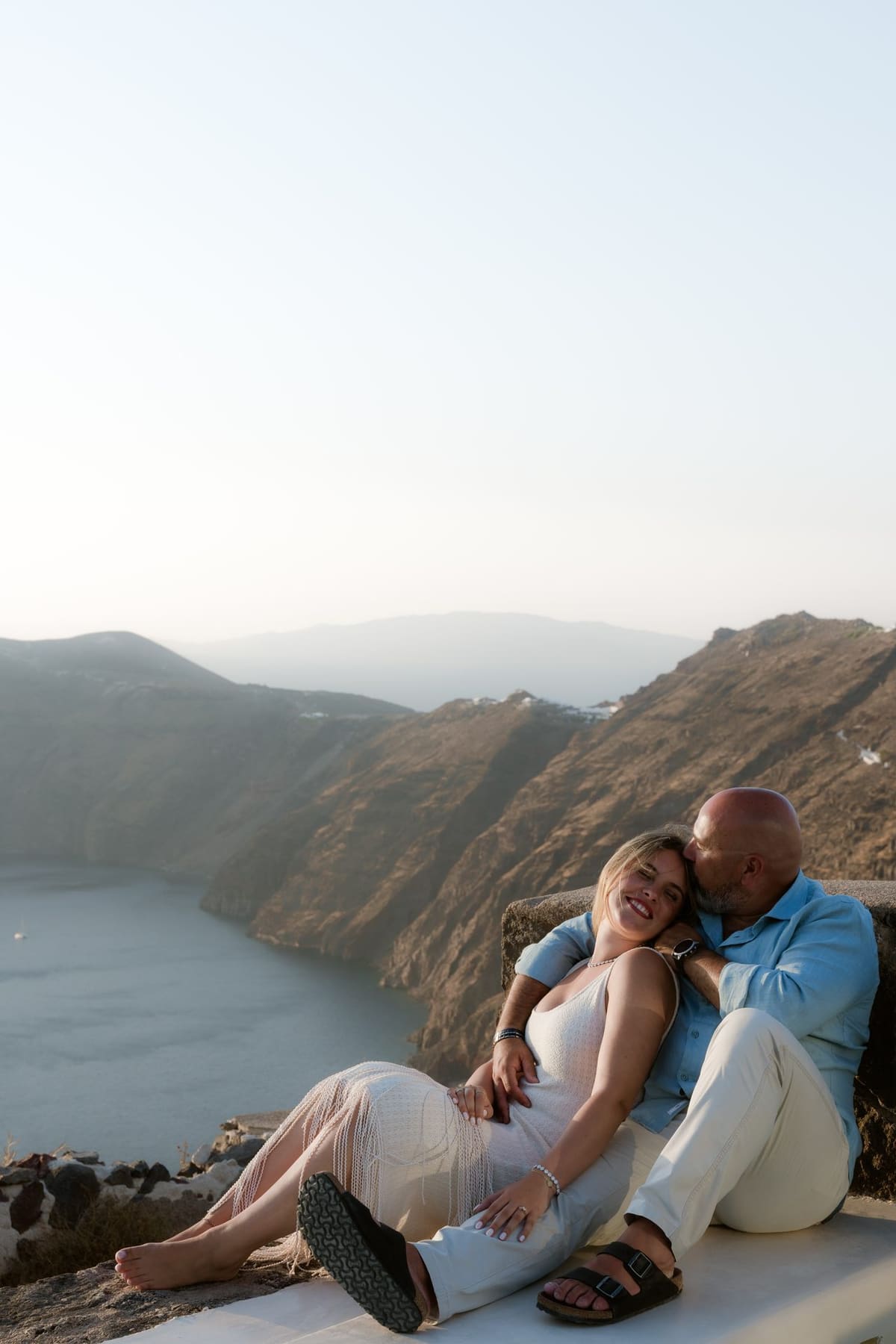 Couple seated on a terrace wall with the caldera at sunset, Imerovigli villa