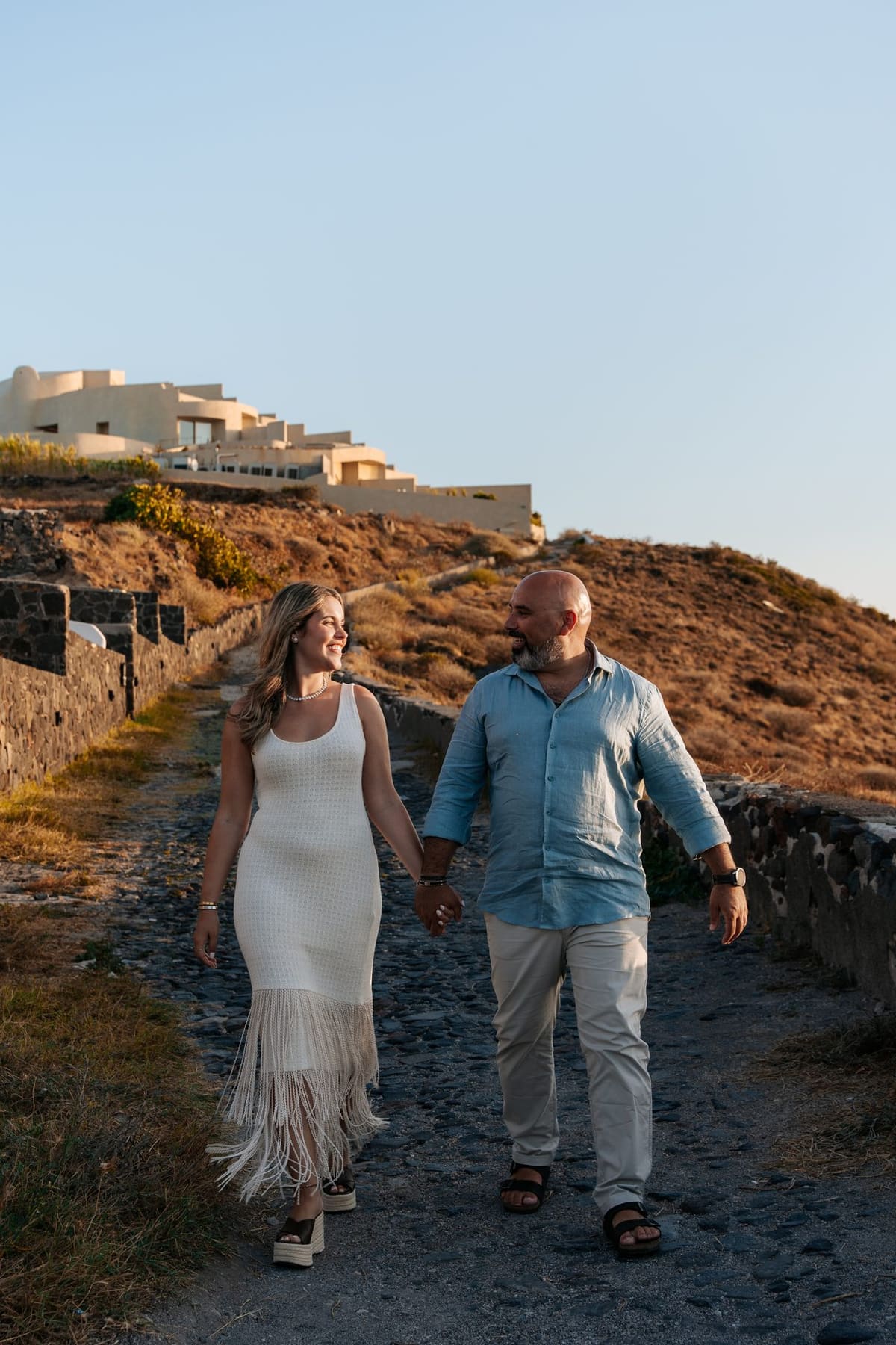 Couple walking hand in hand on the Imerovigli cliff path after the proposal