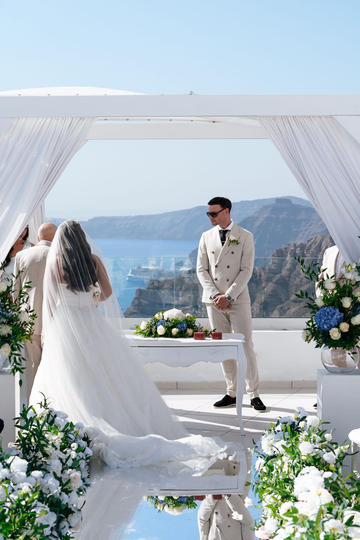 Bride and groom under the white canopy at the end of the mirrored aisle, Santorini