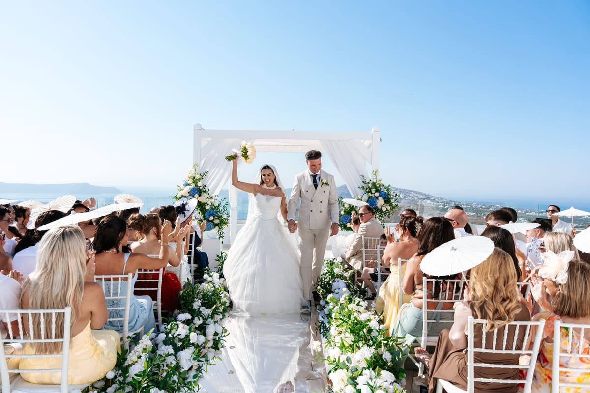 Bride raising her bouquet as the couple walk back down the aisle, Santorini