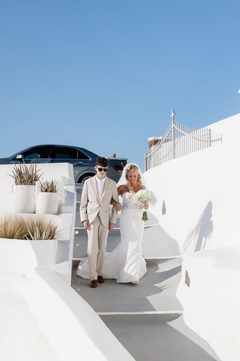Bride and groom walking down the white steps of Imerovigli at dusk after their wedding