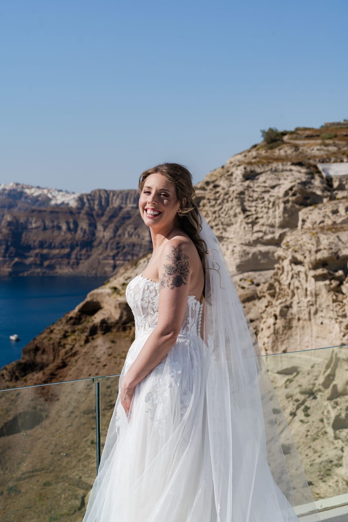 Bride in a tulle gown on a cliff edge with the Santorini caldera behind her