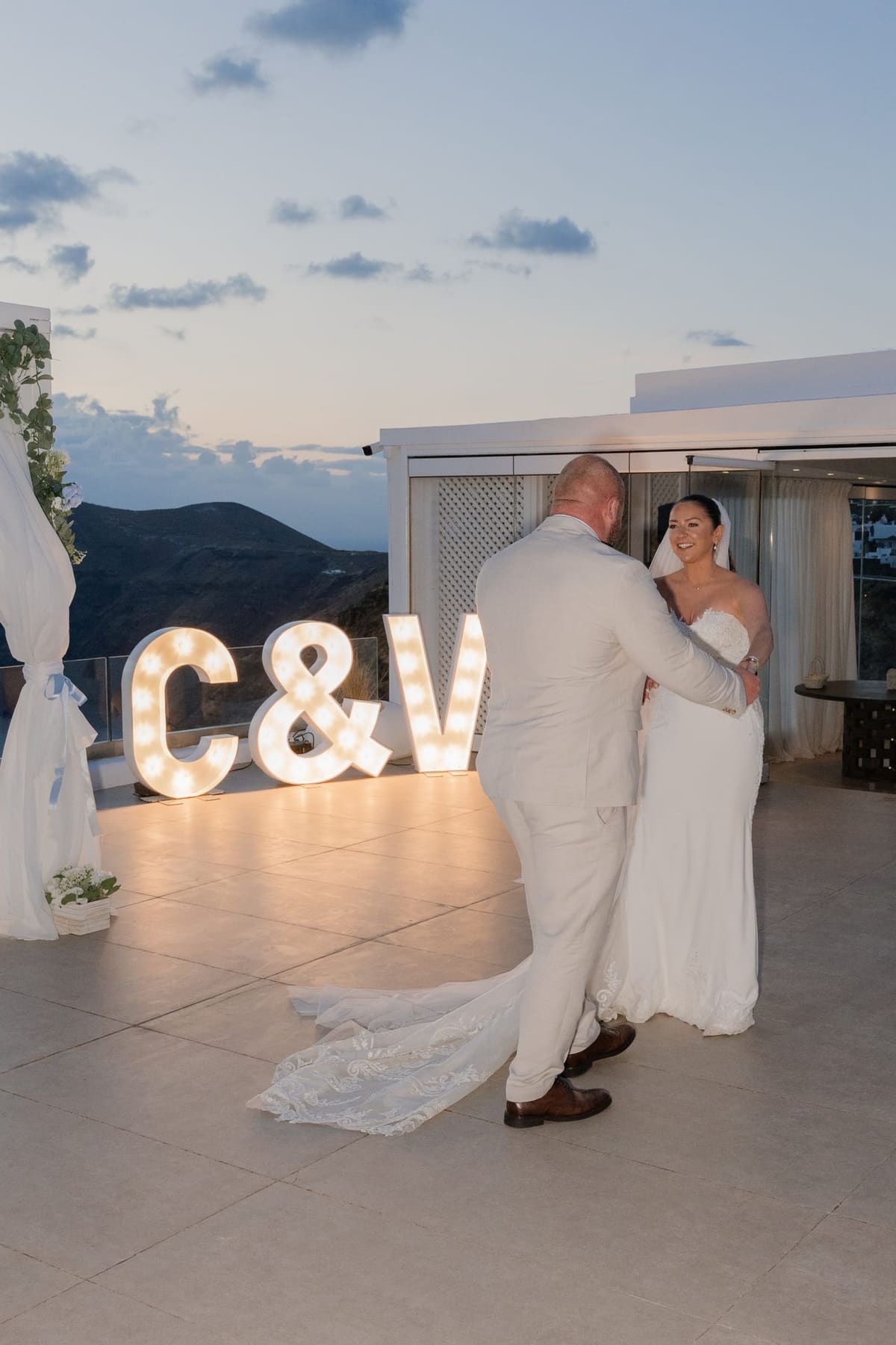 First dance beside lit letters on a terrace above the caldera at blue hour, Santorini
