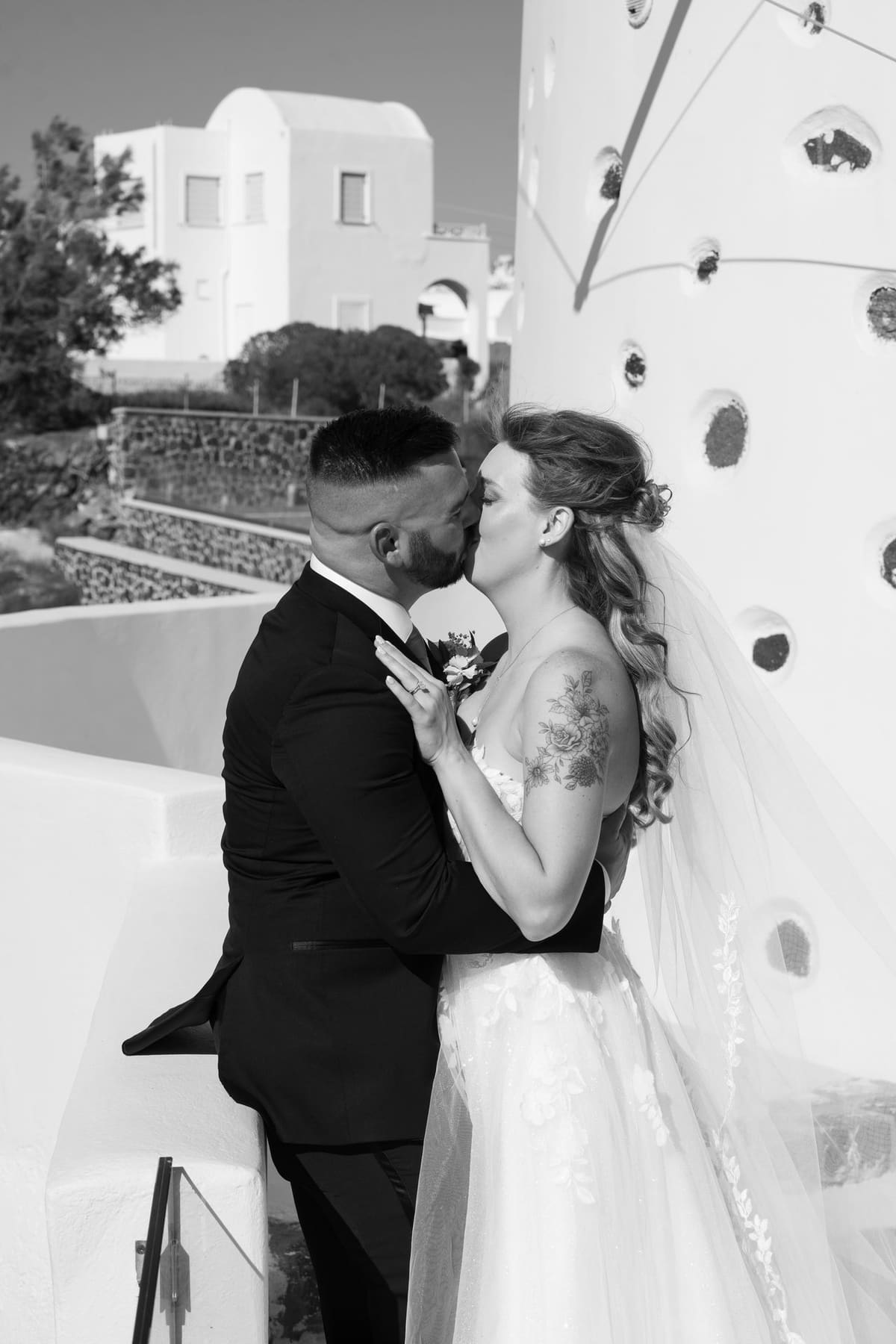 Groom kissing the bride against a white wall, black and white, Santorini wedding