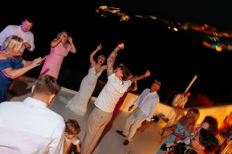 Wedding guests dancing on a Santorini terrace at night with the lights of Fira behind