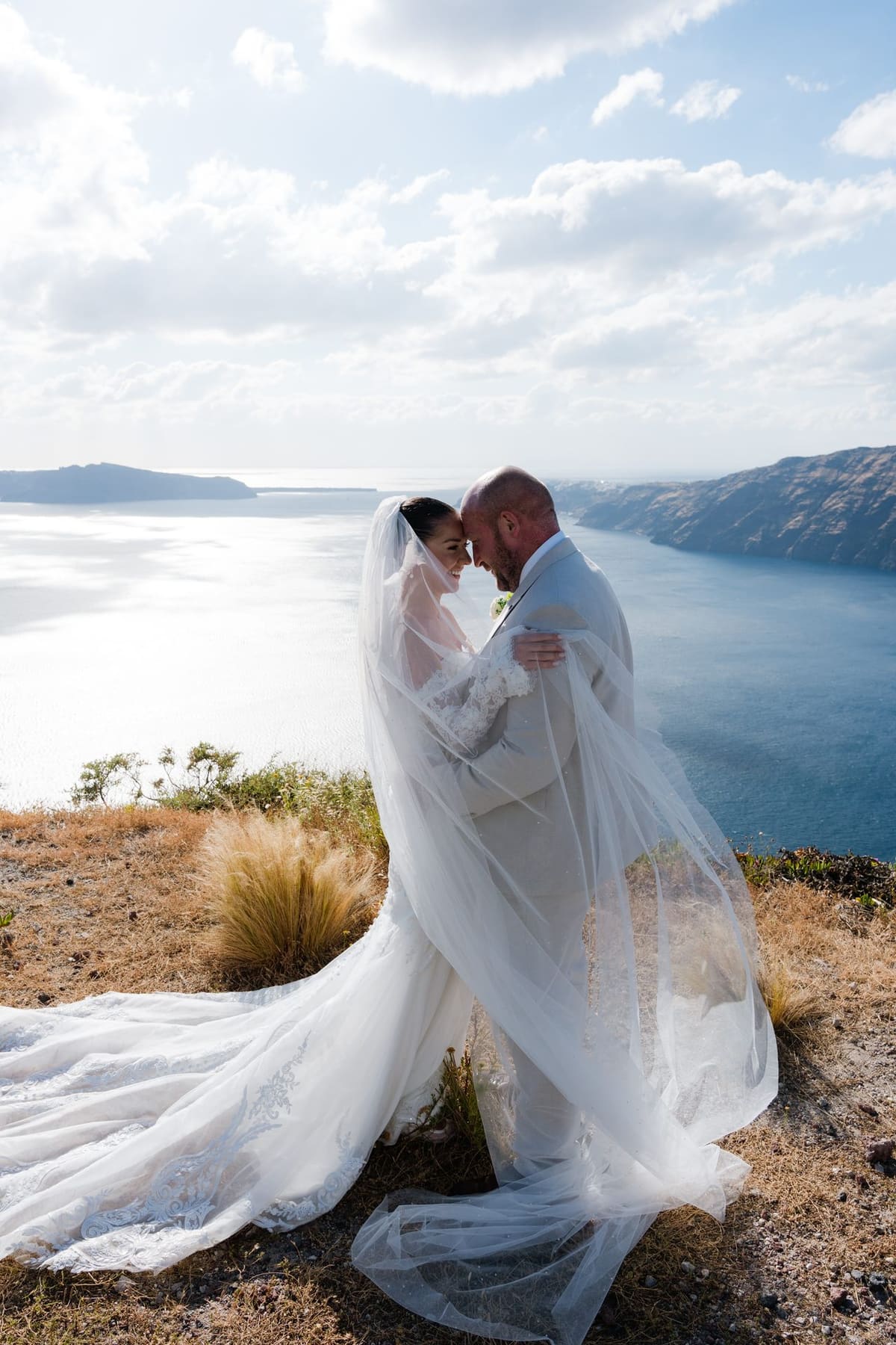 Bride's veil caught by the wind as the couple kiss above the Santorini caldera