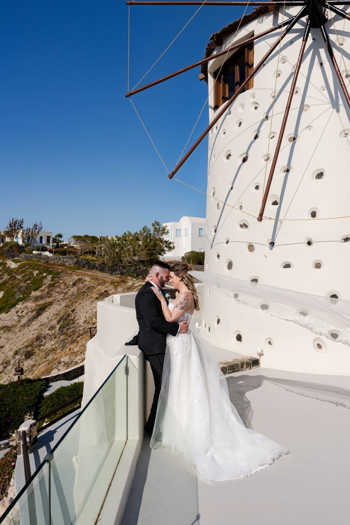 Bride and groom kissing beneath a white Santorini windmill after the ceremony